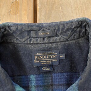 May include: Detail of a blue and green plaid shirt collar. The collar features a dark blue quilted lining and a small tag reading "CANYON". Below, a label states "PENDLETON WOOLEN MILLS" and "XXL".