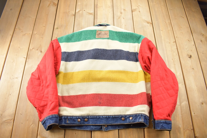 May include: A red and blue striped denim jacket with a multi-colored wool insert. The wool insert has stripes of green, navy blue, yellow, red, and white.