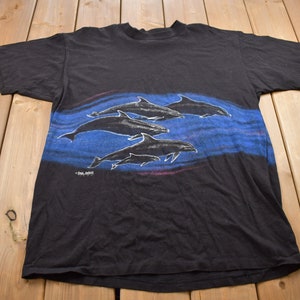 May include: Black t-shirt featuring a graphic print of a pod of dolphins swimming in blue water. The text "Sea Spirit" is printed at the bottom of the design.