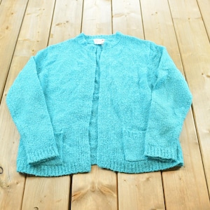 May include: A bright turquoise open-front cardigan featuring a textured knit pattern, long sleeves, and two front patch pockets. The garment has a simple round neckline and a straight hemline, showcasing a consistent solid color throughout the piece.