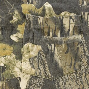 May include: Close-up of a camouflage-patterned shirt with a pocket. The fabric features a mix of green, brown, and tan colours, resembling a forest environment. The pocket is rectangular and sewn onto the shirt.