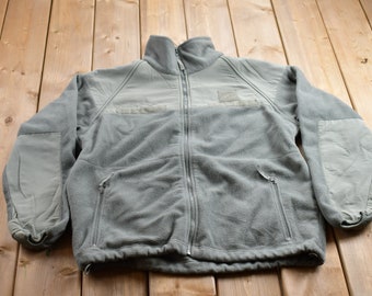 May include: A gray fleece jacket with a zipper closure and two zippered pockets. The jacket has a high collar and a patch on the left chest.