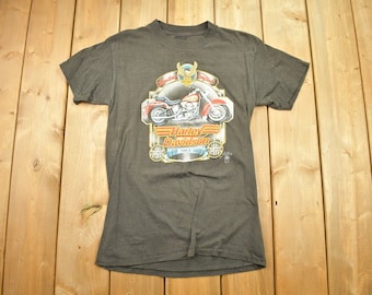 May include: A dark gray t-shirt with a Harley Davidson logo featuring a motorcycle and the text "Harley Davidson" and "100 Since 1903".