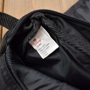 Op de afbeelding: Zwarte ritszak met een rood en wit label met de tekst "The Disney Store" en "Gemaakt in China" in het Engels, Frans en Chinees.