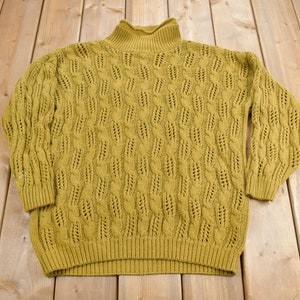 May include: A mustard yellow knitted sweater with a mock neck and a cable knit pattern.