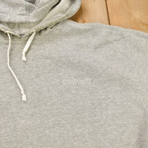 Puede incluir: Sudadera gris con capucha y un logotipo blanco de Carhartt bordado en la parte delantera.