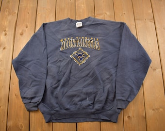 May include: A navy blue sweatshirt with the text "West Virginia Mountaineers" and a diamond-shaped logo with the letters "WV" in yellow and blue.