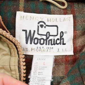 May include: A tan and brown plaid jacket with a zipper closure. The jacket has a label that reads "Henry Hollard Woolrich Est. 1830 St. Morris Ill." and a size tag that reads "33222 L 65% Polyester 35% Cotton Liner 85% Wool 15% Nylon Filling 65% Polyester 35% Polyester Trim - Doyore Fur Origin U.S.A."