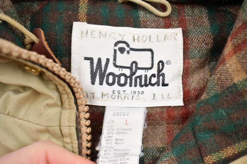 May include: A tan and brown plaid jacket with a zipper closure. The jacket has a label that reads "Henry Hollard Woolrich Est. 1830 St. Morris Ill." and a size tag that reads "33222 L 65% Polyester 35% Cotton Liner 85% Wool 15% Nylon Filling 65% Polyester 35% Polyester Trim - Doyore Fur Origin U.S.A."