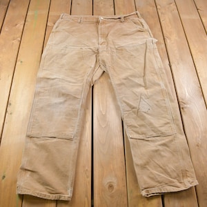 Puede incluir: Un par de pantalones de trabajo de color marr&oacute;n claro con rodillas reforzadas y m&uacute;ltiples bolsillos. Los pantalones est&aacute;n hechos de una tela resistente y duradera y tienen un estilo cl&aacute;sico de trabajo.