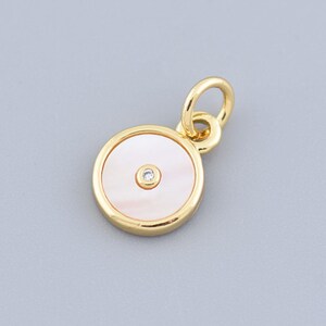 May include: A gold-colored pendant with a round, mother-of-pearl center and a small, clear gemstone. The pendant has a loop at the top for attaching to a chain. The design is simple and elegant.