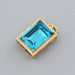 Puede incluir: Colgante rectangular con una gran gema azul claro en el centro. La gema está rodeada por un borde de pequeñas piedras transparentes engastadas en un marco de metal dorado. Un pequeño lazo en la parte superior para una cadena.