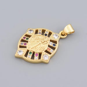 May include: Gold-colored pendant with a religious figure in the center, surrounded by colorful gemstones and clear crystals. The pendant has a rectangular shape with a decorative border and a loop for a chain.