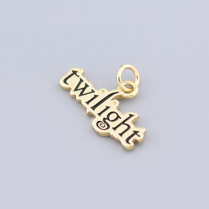 Puede incluir: Encanto de color dorado con la palabra "twilight" en letras negras. El encanto tiene un bucle en la parte superior para sujetarlo a un collar o pulsera.