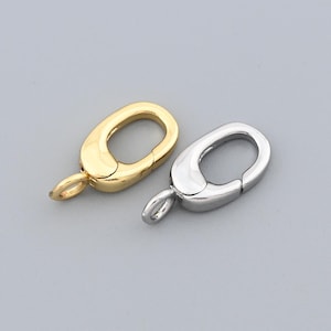 May include: Two oval-shaped jewelry clasps. One is gold-toned, the other is silver-toned. Each clasp has a small loop at one end for attachment. The clasps are set against a plain gray background.