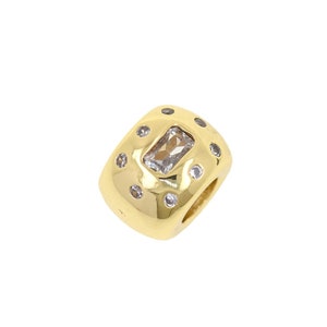 May include: Gold charm with a rectangular clear stone surrounded by smaller clear stones.
