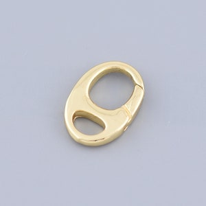 May include: A gold-toned metal clasp with a rounded oval shape. The clasp has a spring-loaded mechanism for attaching to a chain or other jewelry.