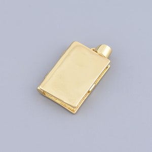 May include: A gold-coloured flask pendant with a rectangular body and a small, cylindrical top. The pendant has a smooth, reflective surface and is set against a grey background. The flask appears to be made of metal.