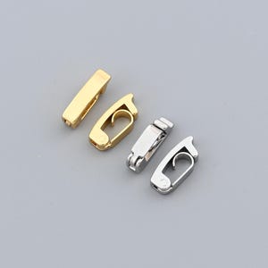 May include: Four metal clasps in gold and silver tones are arranged on a gray background. Two are gold, one rectangular and one with a curved hook. The other two are silver, with a similar hook design. These clasps are likely for jewelry or small accessories.