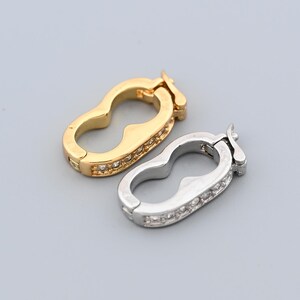 May include: Two decorative jewelry clasps. One is gold-toned, the other is silver-toned. Both clasps have a unique, curved shape and are embellished with small, clear gemstones. The clasps are designed to secure jewelry pieces.