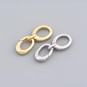 Può includere: Due chiusure metalliche, una dorata e una argentata, sono mostrate su uno sfondo grigio. Ogni chiusura ha una forma ovale con un'apertura a cerniera. Le chiusure sono progettate per la creazione di gioielli o altri progetti artigianali.