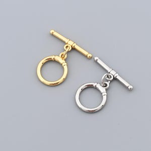 Pode incluir: Duas fechos de alternância de metal. Um é dourado, o outro prateado. Cada fecho tem um anel circular e uma barra em forma de T. Estes fechos são projetados para fazer joias e artesanato.