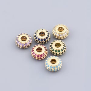 May include: Seven gold-toned round beads with different colored gemstones. The beads are all the same size and have a small hole in the center.