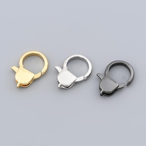 May include: Three metal lobster clasps in gold, silver, and gunmetal gray. Each clasp features a rounded ring and a lever-activated closure. The clasps are designed for jewelry making and crafting projects.