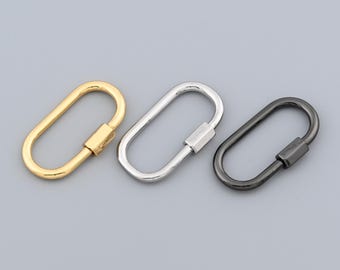 Könnte beinhalten: Drei ovale Schraubkarabinerverschlüsse in Gold, Silber und Schwarz. Die Metallverschlüsse haben einen Schraubmechanismus für einen sicheren Verschluss. Die Verschlüsse werden auf grauem Hintergrund gezeigt.