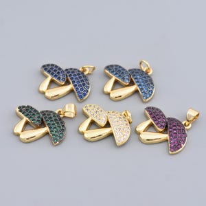May include: Five gold-colored mushroom pendants with colorful gemstone caps. The caps are blue, green, white, and purple. Each pendant has a loop for attaching to a chain or bracelet. The mushrooms are set against a gray background.