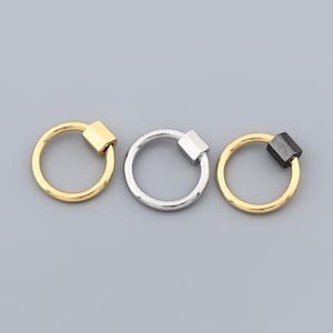 Puede incluir: Tres cierres de mosquetón metálicos en dorado, plateado y negro. Cada cierre tiene un anillo circular con un mecanismo de bloqueo de forma cuadrada. Los cierres se muestran sobre un fondo gris.