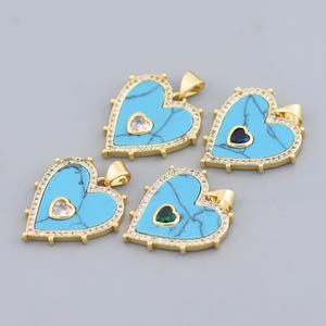 May include: Four heart-shaped pendants with turquoise centers and gold-colored frames. Each pendant has a small heart-shaped gemstone in the center. The frames are encrusted with small, clear gemstones. The pendants are displayed on a gray background.