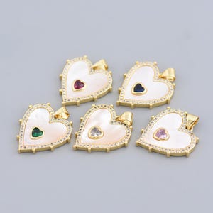 May include: Gold-tone heart pendants with a mother-of-pearl finish. Each pendant features a small heart-shaped gemstone in red, blue, green, clear, or pink. The edges are adorned with small, clear crystals.