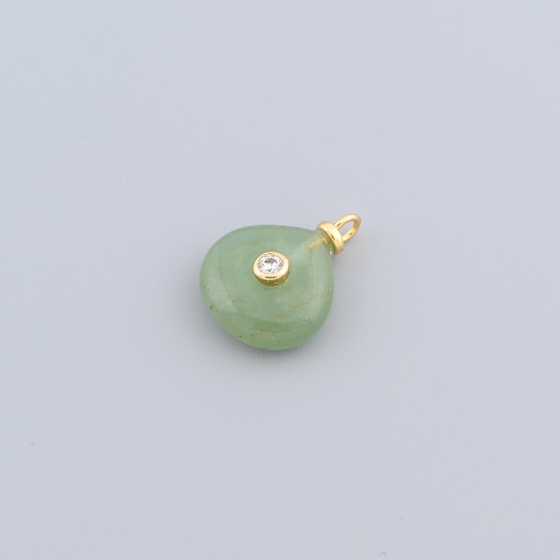 May include: A light green, teardrop-shaped pendant with a gold-coloured bail. The pendant has a small, round, clear gemstone set in the centre. The bail is also gold-coloured.