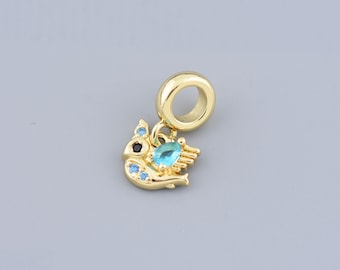 May include: A gold-colored charm with a bird design, featuring a black eye and blue and turquoise accents. The charm has a loop at the top for attaching to a bracelet or necklace. The bird has a wing and is embellished with small blue stones.