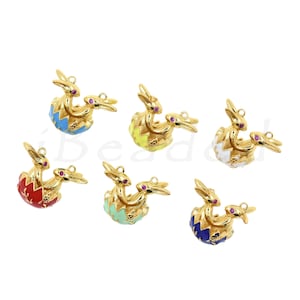 Op de afbeelding: Goudkleurige metalen bedels met een konijn dat uit een kleurrijk ei komt. Elke bedel heeft een andere eierkleur: blauw, geel, rood, mintgroen, wit en donkerblauw. De konijnen hebben rode edelsteenogen.