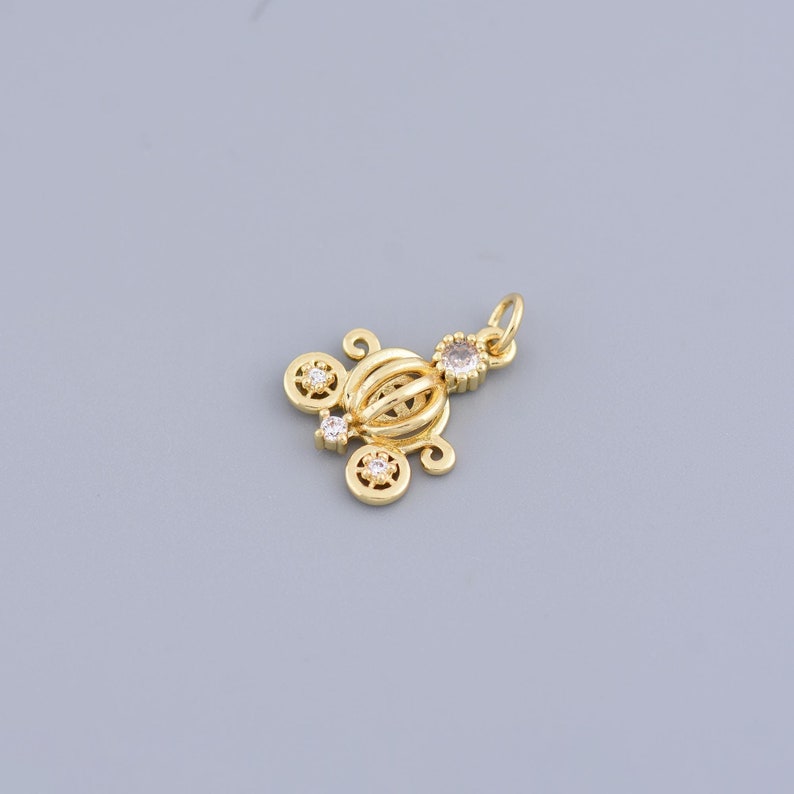May include: Gold-tone carriage charm with clear crystal accents. The charm is detailed with a rounded top and a decorative design.