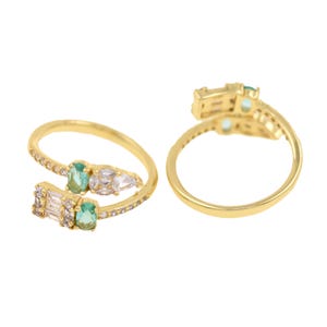 May include: A gold ring with a delicate design featuring green and white stones. The ring is open and adjustable to fit different finger sizes.