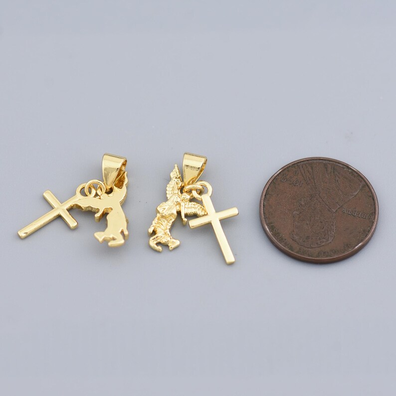 May include: Two gold-colored pendants with religious themes. One pendant features a cross and a stylized angel, while the other has a cross and a figure. A coin is next to the pendants.