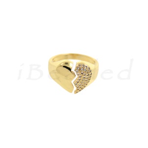 May include: Gold ring with a broken heart design. One half of the heart is solid gold, while the other half is covered in clear rhinestones.