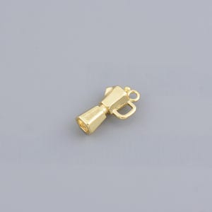 May include: A gold-colored charm in the shape of a coffee maker, featuring a handle and a loop for attaching to a bracelet or necklace. The charm has a polished finish and is set against a gray background.