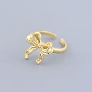 Puede incluir: Un anillo ajustable de color dorado con un diseño de lazo.