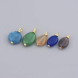 May include: Five gemstone pendants in a row, each with a gold-coloured bail. The gemstones are in shades of blue, green, orange, dark blue, and grey. The pendants are oval or round, and the gold bails are small and looped.