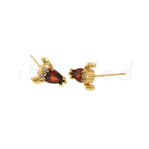 May include: A pair of gold-tone earrings featuring a red gemstone and a small crab design.