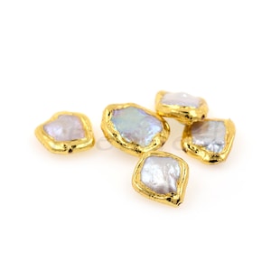 May include: Five irregular shaped white pearl beads with gold metal trim. The beads are scattered on a white surface.