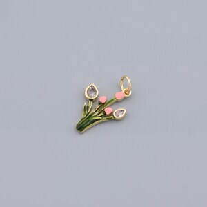 Puede incluir: Un colgante dorado con forma de ramo de flores. El ramo presenta capullos rosas, hojas verdes y detalles transparentes en forma de lágrima. El colgante tiene un pequeño lazo para sujetarlo a una cadena.