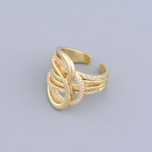 May include: A gold ring with a unique, intricate design featuring multiple intertwined bands adorned with small clear stones.