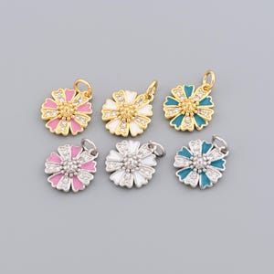 Può includere: Sei ciondoli a forma di margherita in tonalità oro e argento. I ciondoli presentano petali in smalto bianco, rosa e turchese con un gruppo centrale di cristalli trasparenti. Ogni ciondolo ha un piccolo anello.