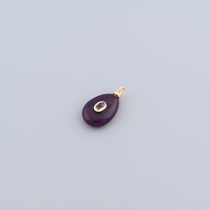 May include: A teardrop-shaped pendant with a deep purple hue, featuring a small, oval-shaped gemstone in the center. The pendant has a gold-colored bail for hanging. The gemstone is surrounded by a gold-colored setting.