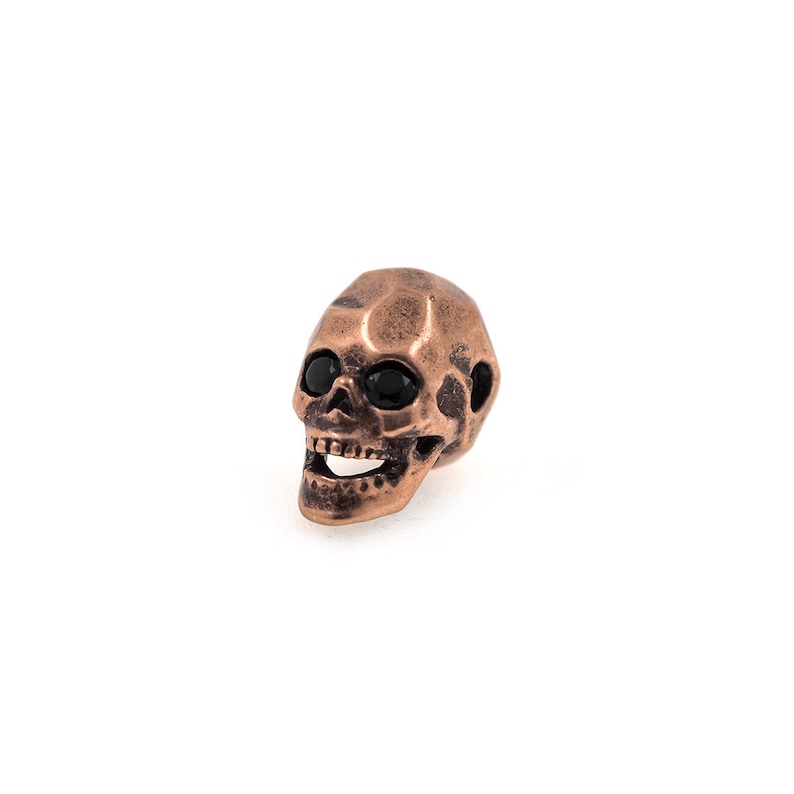 May include: A small, copper-colored skull with black eyes. The skull is detailed with a toothy grin and a textured surface.